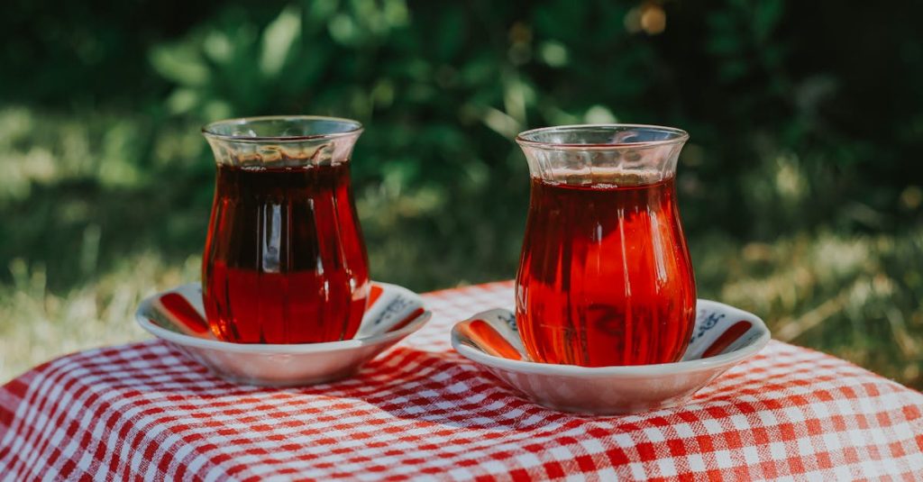 Two glasses of Turkish tea on a checkered picnic tablecloth outdoors.