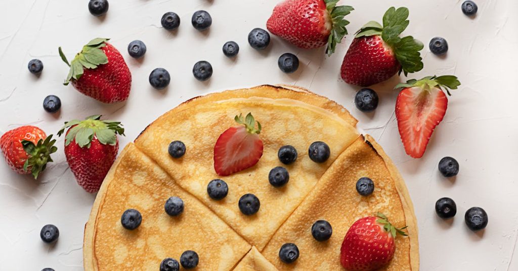 Mouth-watering crepes topped with fresh strawberries and blueberries on a white table.